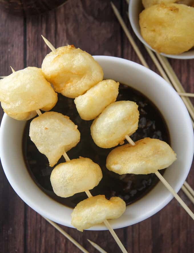 fried fish balls skewered in bamboo sticks on top of a bowl of fish ball sauce.